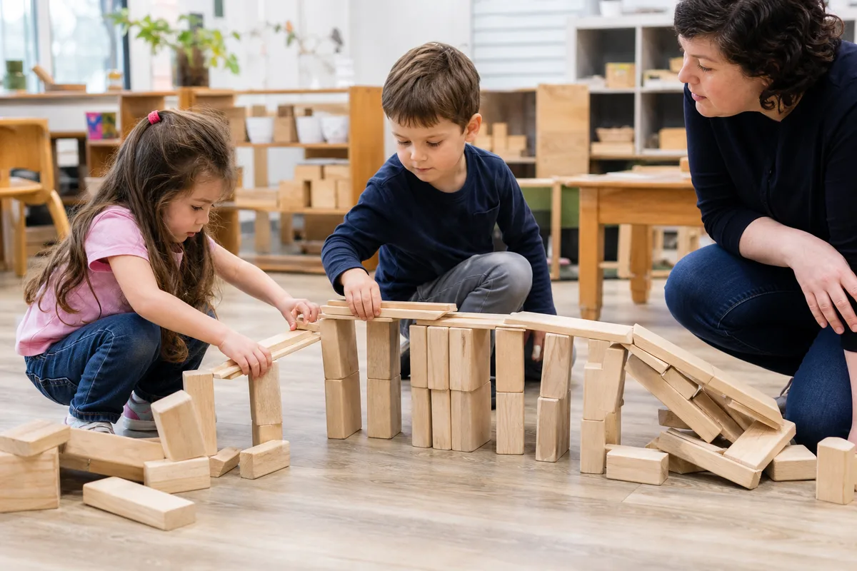 Preschool children rebuilding a wooden block bridge with an educator nearby