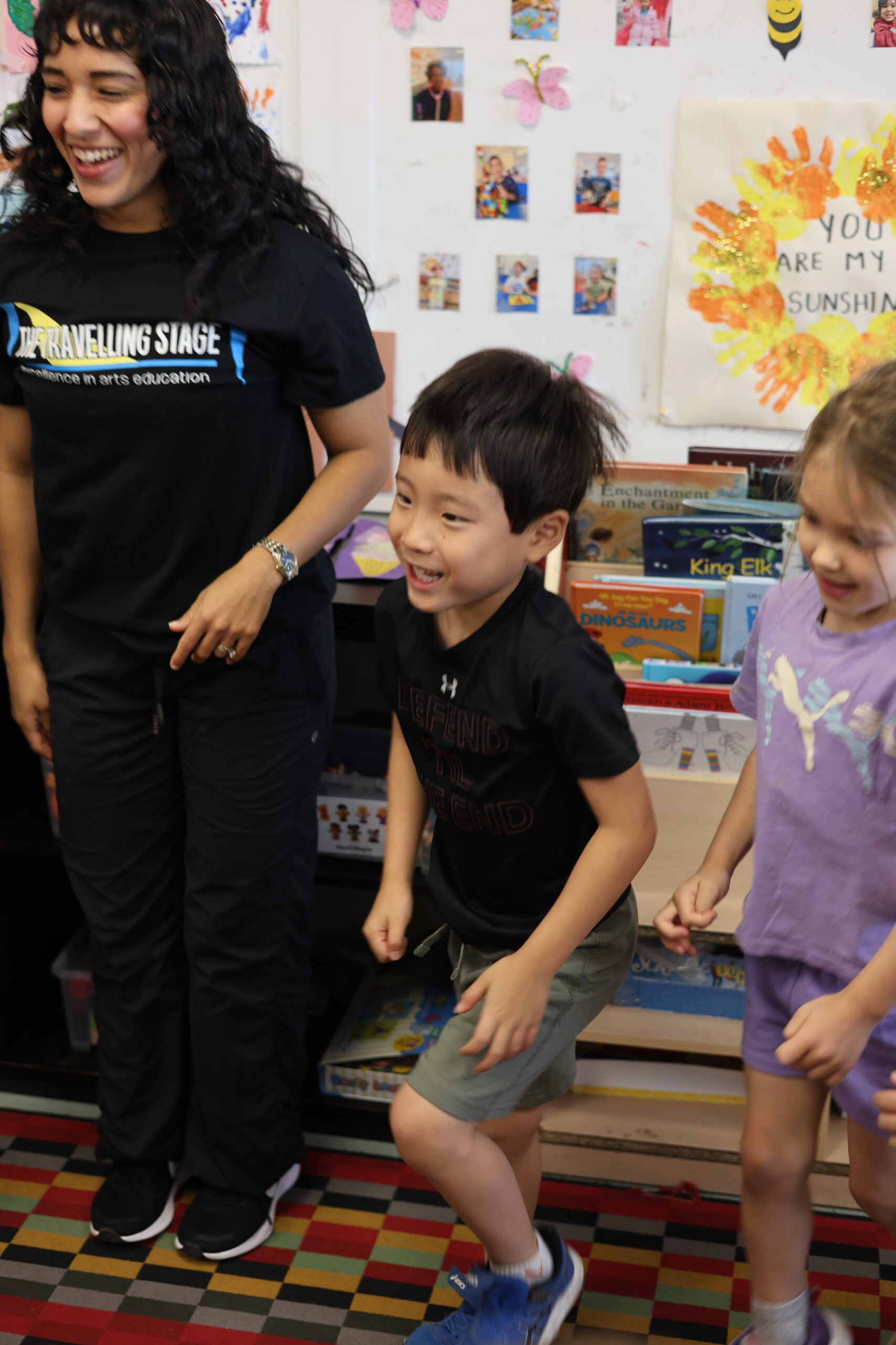 An adult and children smiling as they move together in a classroom