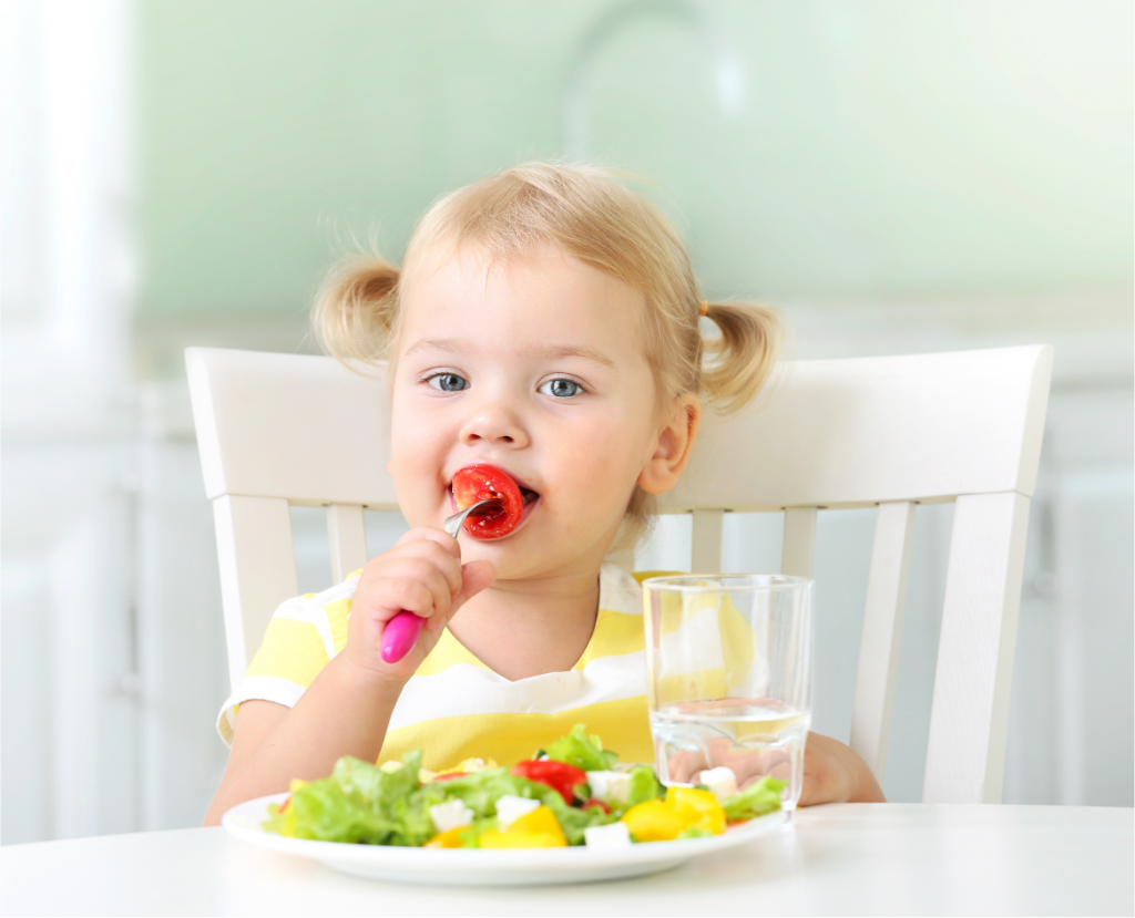 Toddler eating healthy salad at a table